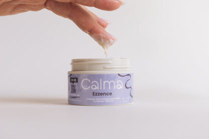 Hand applying cream from a jar labeled 'Calm A Ezzence' on a light background