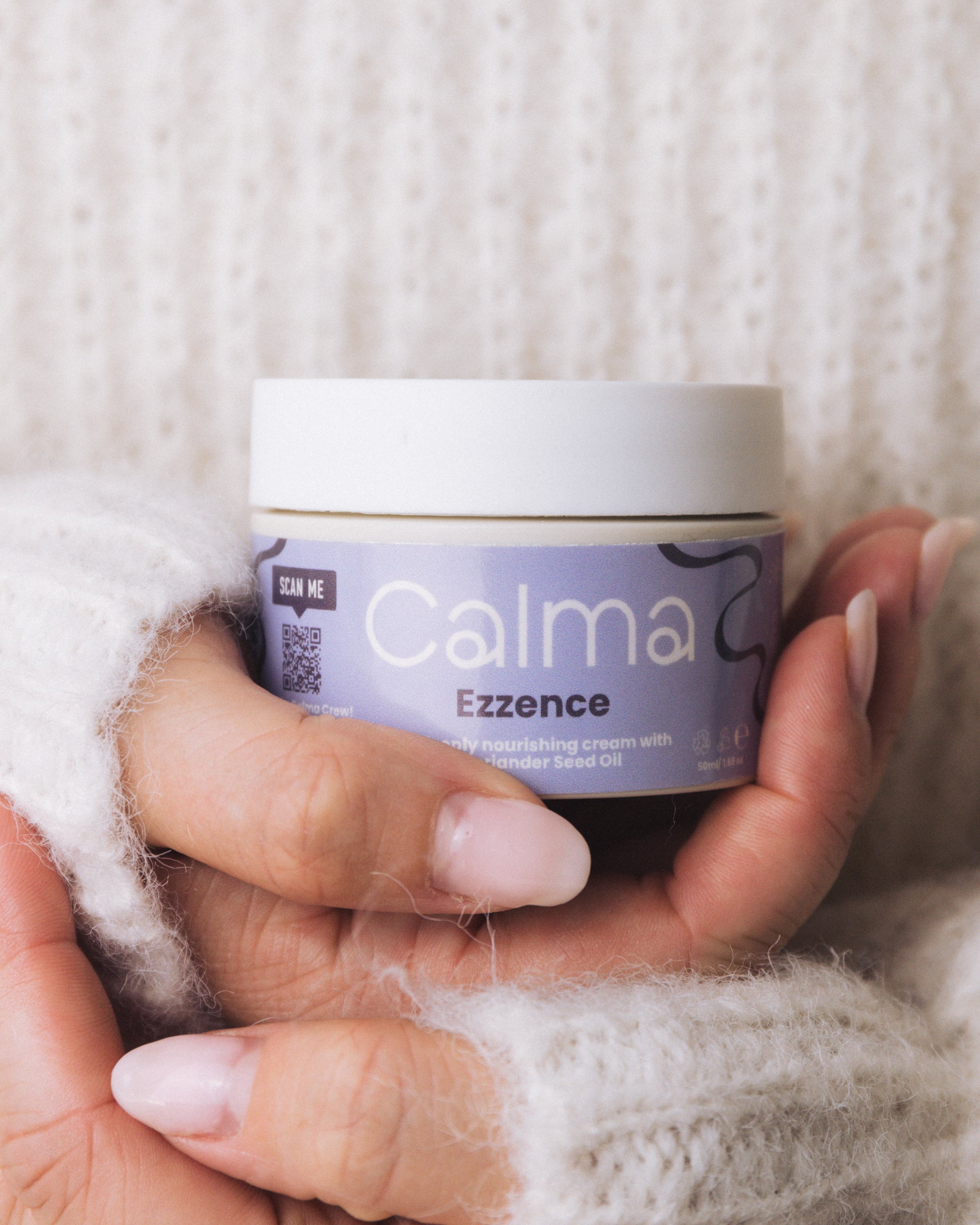 Hand holding a jar of Calma Ezzence cream against a textured white background