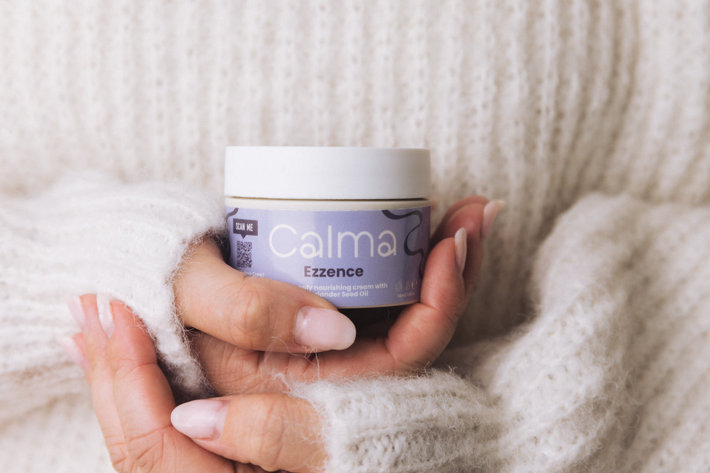 Hand holding a jar of Calma Ezzence cream against a soft, neutral background