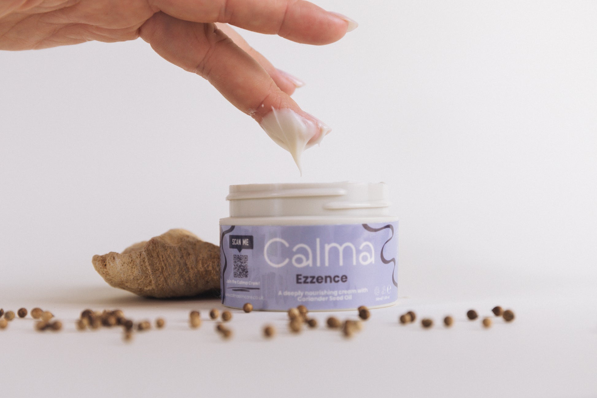 Hand holding a white object above a jar labeled 'Calma Ezzence' on a light background