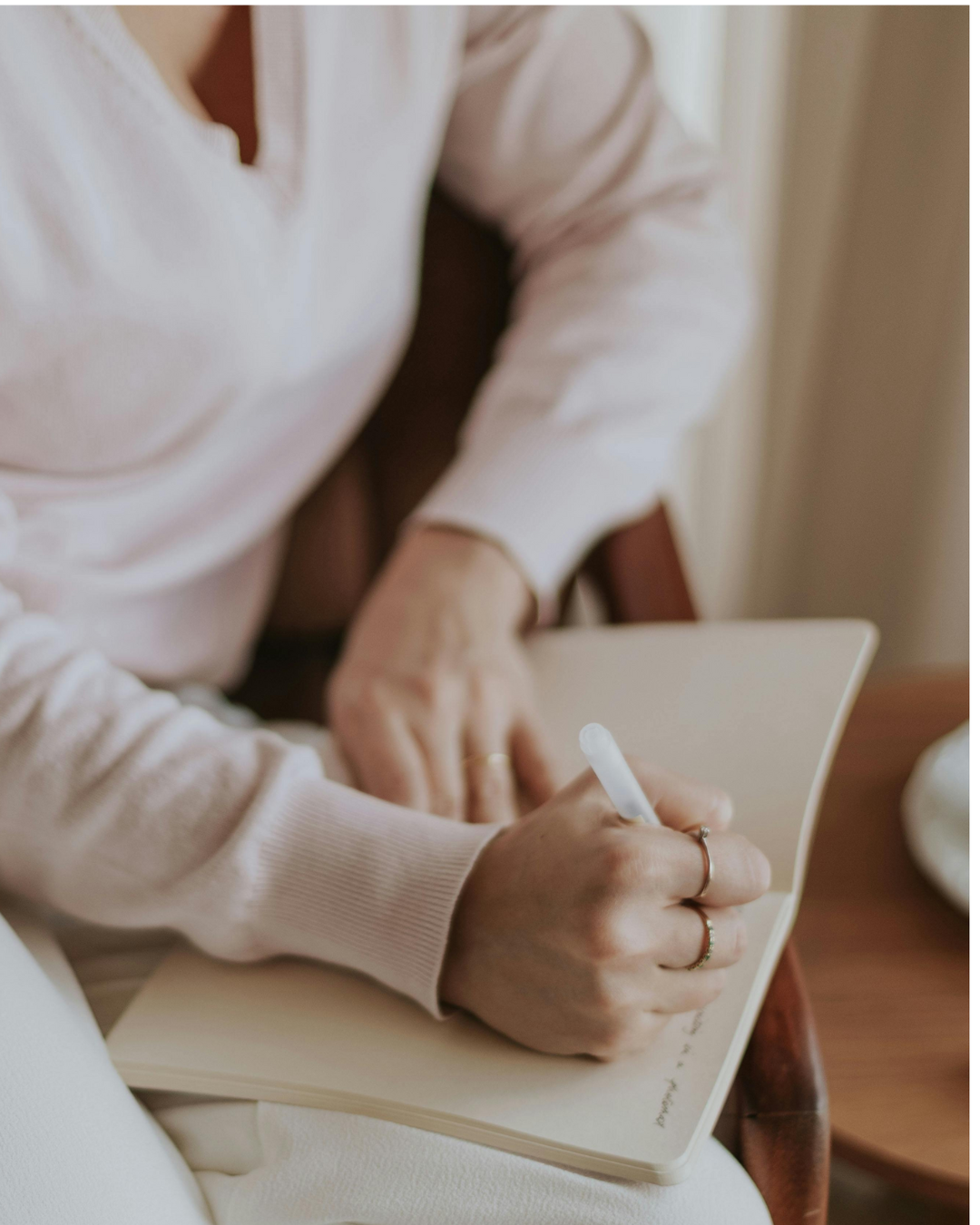 Person writing in a notebook with a pen, wearing a light pink sweater.
