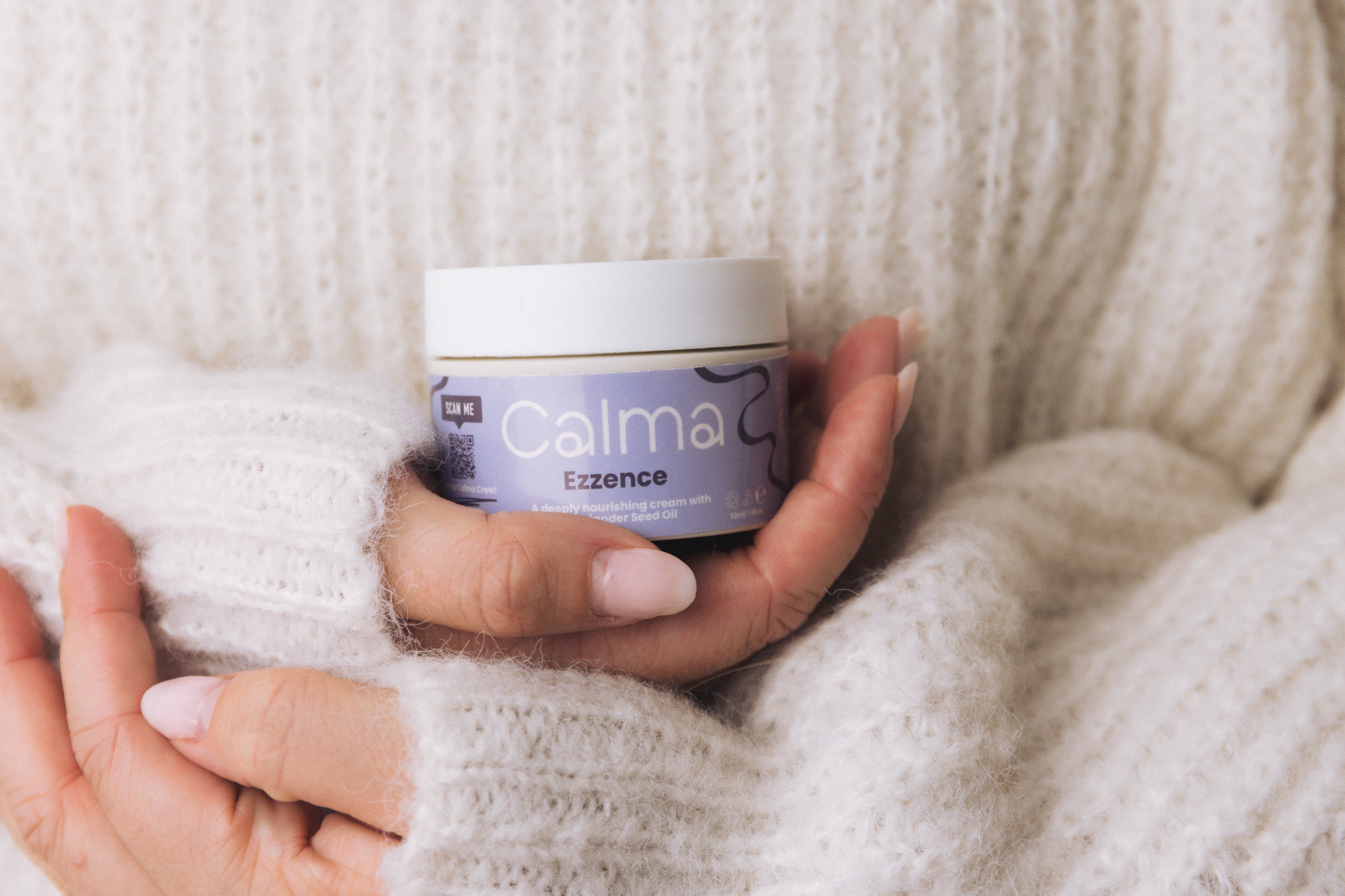 Person holding a jar of Calma Ezzence cream against a soft, neutral background